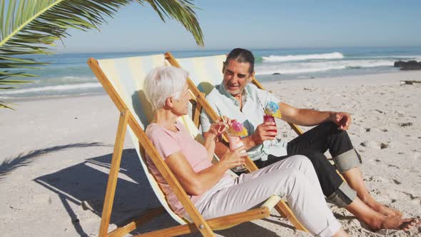 Senior Caucasian couple sitting on sunbeds at the beach.
