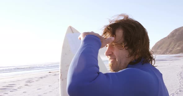 Surfer with surfboard shielding eyes at beach