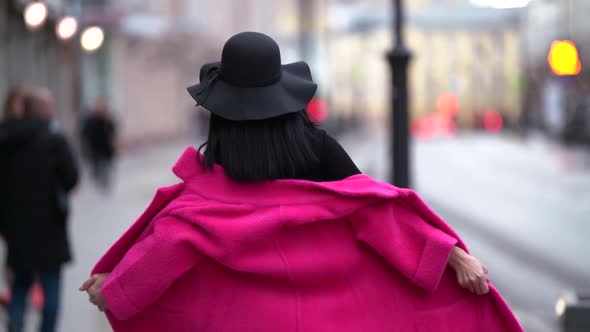 Fashionable Glamorous Young Woman with Black Hair, Black Hat and Purple Coat Walks Down the Street