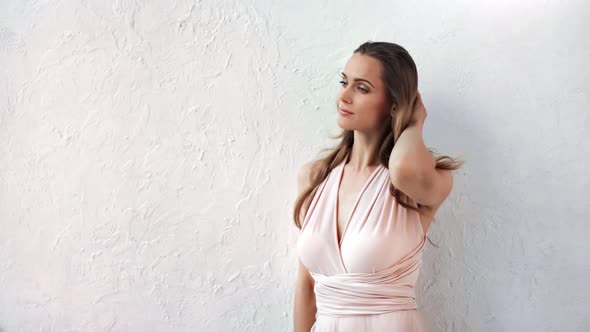 Beautiful Fashion Woman in Tender Pink Dress Playing Hair