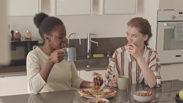 Happy Lesbian Couple Eating Homemade Sandwiches at Kitchen Table