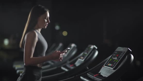 Female Athlete Run on a Treadmill and Uses a Smartphone To Tracks Sports Activity Aerobic Exercise