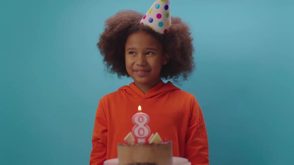 African American girl in birthday hat blowing out number 8 candle