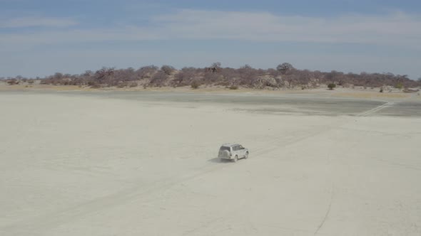 Traveling SUV Car On Arid Desert At Kubu Island, Botswana With Baobabs And Salt Pan In Background. A