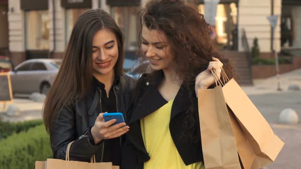 Girl Shows Her Friend Something on Her Smartphone on the Street of the City