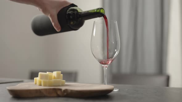 Slow Motion Pour Red Wine Into Wineglass with Hard Cheese on Background on Wood Table