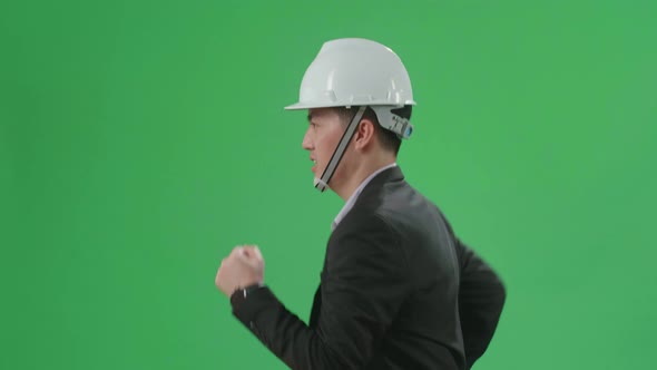 Side View Of Asian Chief Engineer In The Hard Hat Runs On Green Screen Chroma Key