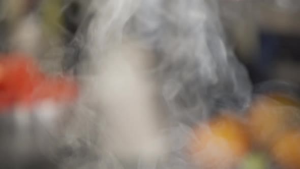 Steam rising from a pot or pan in slow motion while cooking. Kitchen out of focus behind the steam.