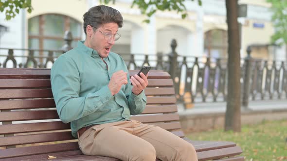 Man having Success on Smartphone Sitting on Bench