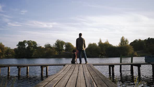 Man with Dog Standing on the Edge of the Pier Admiring the Beauty of the Lake
