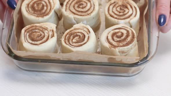 A Woman Demonstrates Sliced Cinnamon Dough For Baking Cinnabons. In A Baking Dish. Close Up Shot.