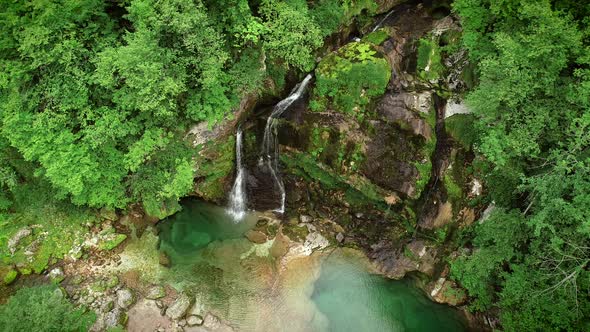 Aerial view of the top of a small waterfall with clean water downhill.