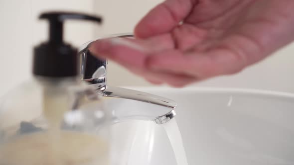 young man disinfects his hands with liquid soap and water in a sink with a mixer in the bathroom