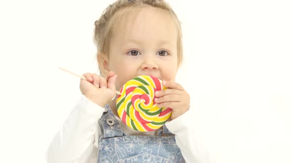 Little Girl Is Holding a Sweet Candy in Her Hands and Licks It. White Background