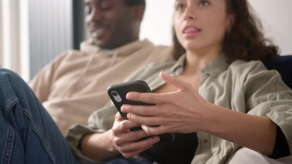 Close Up Of Young Couple Relaxing At Home On Sofa Checking Social Media On Mobile Phones Together