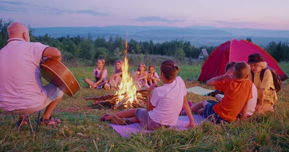 Happy Teenagers Sitting Around Campfire Singing Songs with Guitar