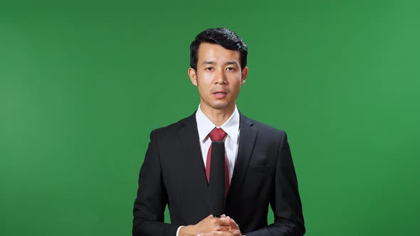 Asian Male Tv News Reporter In Formal Wear Talking On A Green Screen, Chroma Key