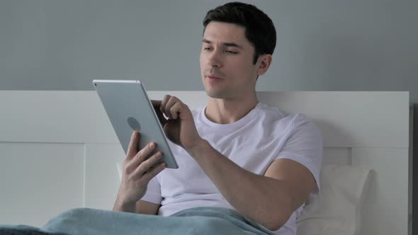 Young Man Browsing Internet on Tablet in Bed