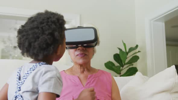 Happy african american grandmother using vr headset with granddaughter in living room