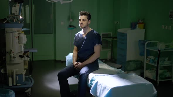 Wide Shot Portrait of Serious Male Confident Surgeon Sitting on Medical Couch in Operating Room As