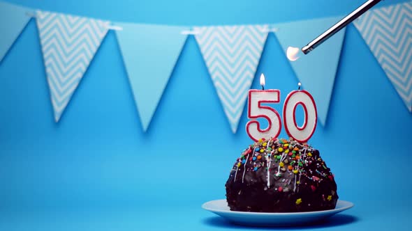 chocolate birthday cake with a burning candle number fifty, 50 on a blue background. Copy space. pla