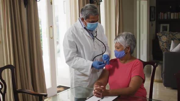 Male doctor visiting senior mixed race woman using stethoscope