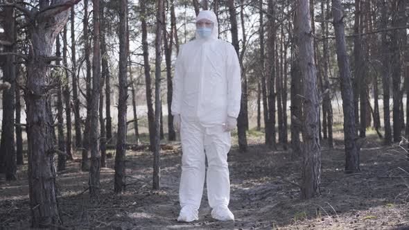 Conscious Caucasian Young Man in White Safety Suit Standing in Forest Next To Suburban Road and