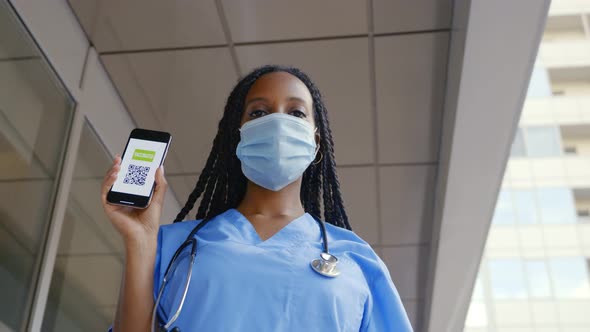 Low Angle View of Afro Female Doctor in Medical Mask Show Digital Vaccinated Passport on Smartphone