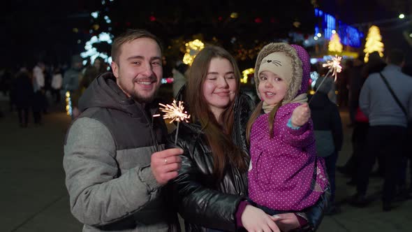 A happy family with a child waves sparklers on New Year's Eve on the street