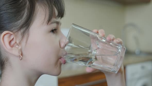 A child in the kitchen drinks water. 