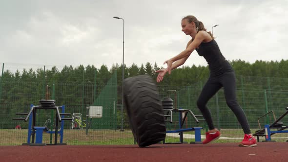 Side View of a Strong Woman Pushing a Tire During an Outside Workout