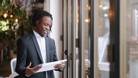 Businessman Standing and Reading Reports in the Cafe