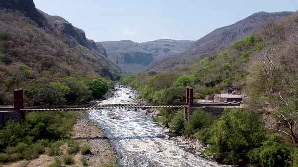 Aerial drone flying over a suspension bridge along a river in the Barranca de Huentitan National Par