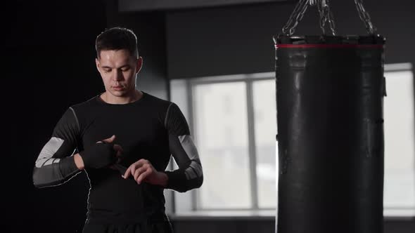 Athletic Young Man Boxer Bandaging His Hands Standing Near the Punching Bag