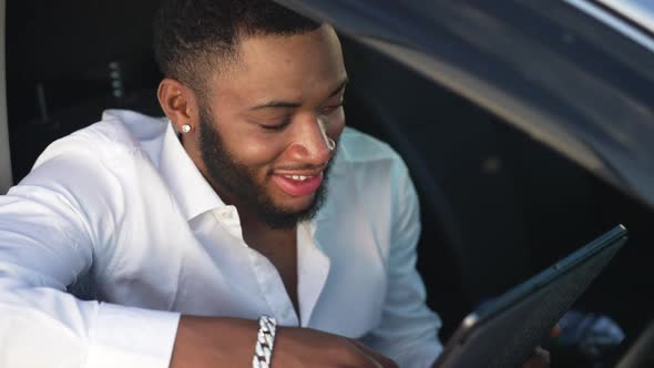 Smiling Gay Man Reading Messages in Social Media Using App on Tablet Sitting in Car