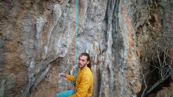 Slow Motion of Joyful Handsome Man Rock Climber in Yellow Sweatshirt with Long Hair Hanging on Rope