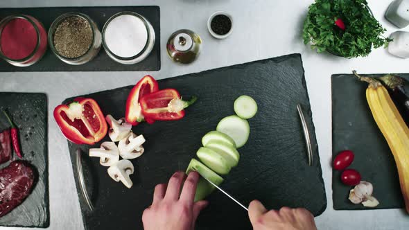 Slow motion footage of a chef cutting vegetables on a black cutting board in the kitchen