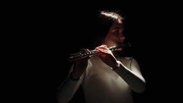 Beautiful Brunette Girl Picks Up a Flute Puts It to Her Lips and Starts Playing on a Black