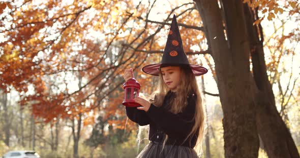 Cute Little Girl with Long Hair Looking Like a Witch in a Special Dress and Hat in the Autumn Forest