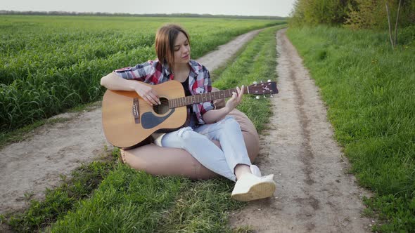 Woman Plays Music on Guitar and Sings on the Country Road Near Wheat Field