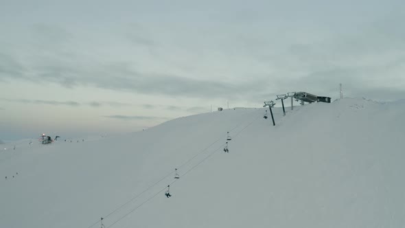 Chairlift transporting winter enthusiasts to top of mountain, wide establishing shot.