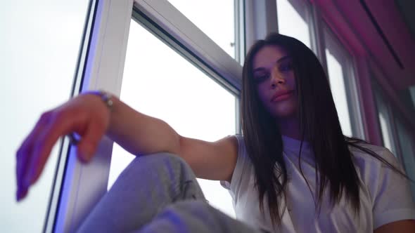 Beautiful Girl is Sitting on the Windowsill Smiling and Looking at the Camera