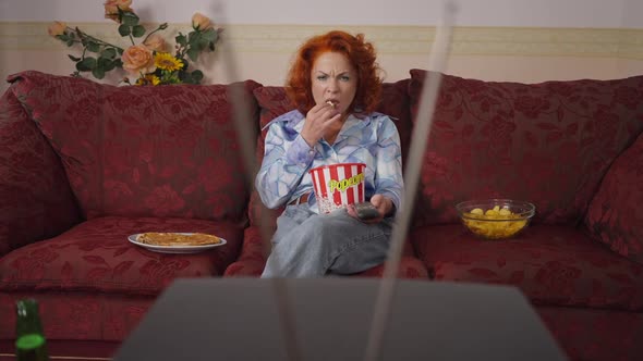 Absorbed Caucasian Retro Woman Switching Channels Eating Popcorn Watching TV at Home