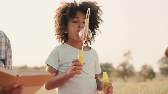 A small afro-american girl is blowing bubbles