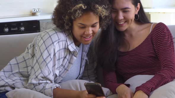 Two Girlfriends Looking at a Smartphone While Sitting on the Couch