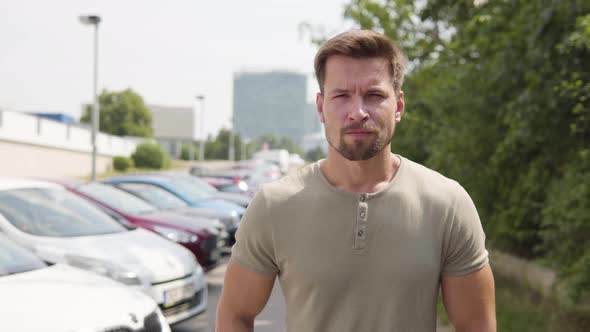 A Young Handsome Man Looks Seriously at the Camera in a Parking Lot in an Urban Area