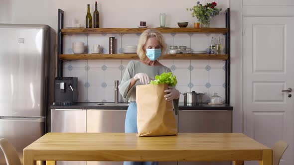 Mature Woman in Safety Mask Unpack Delivery Bag with Food