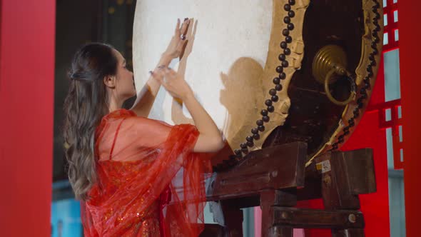 Beautiful Asian woman wearing a traditional red Chinese dress beats the large drum to celebrate the