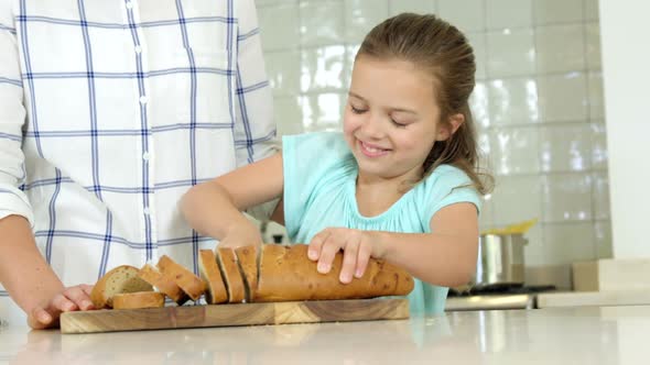 Mother assisting daughter in cutting bread loaf