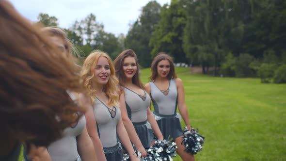 Portrait of Attractive Cheerleaders Standing in Row, Raising Hands with Pompons and Spinning Around